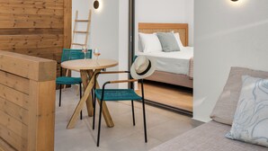 A room with a wooden wall, a round table with chairs, a bed with pillows, and a window. - NOIMA Casa Unico (Agistri)