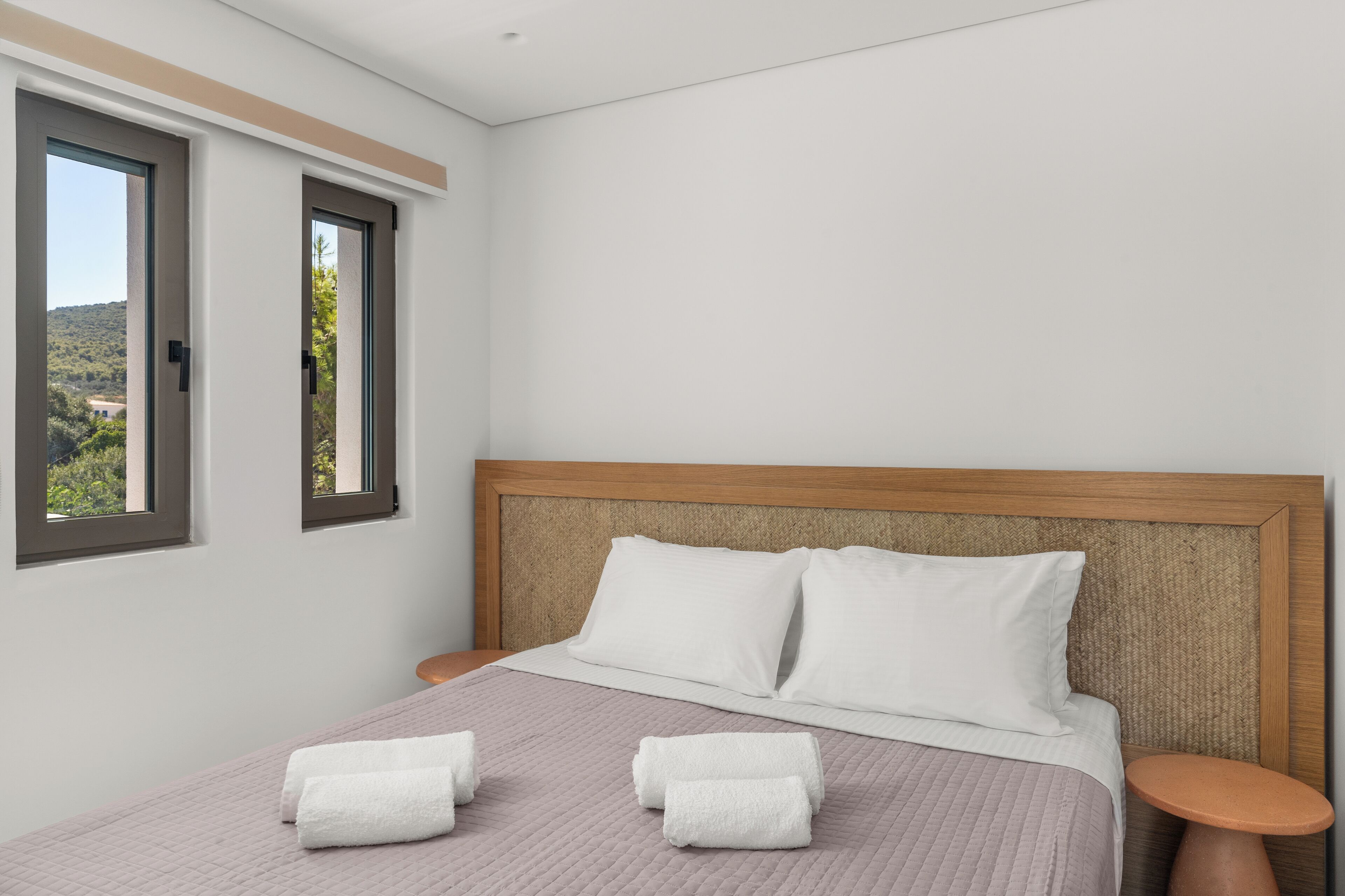 A neatly made bed with two pillows and two folded towels, a wooden headboard, and two bedside tables.
