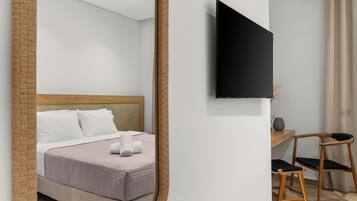 Un dormitorio moderno con una cama, un televisor montado en la pared, un escritorio con una silla y una pared decorativa de ladrillo.