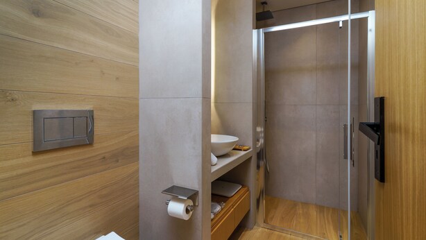 A modern bathroom with a wooden panel wall, a built-in shelf with a laptop, a toilet paper holder, and a shower area. - NOIMA Casa Unico (Agistri)