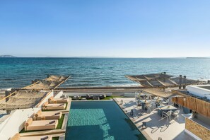 Zona de piscina en la azotea con asientos y mesas, con vistas al mar.