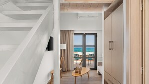 A modern hotel room with a staircase, a wooden floor, a sofa, a table with decorative items, and a view of the sea through a glass door. - NOIMA Casa Unico (Agistri)