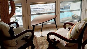 A room with a view of the sea through large windows, a wooden chair, a small table, and a woven chair. - Apartamento Junto al Mar, Wi-fi Gratis. Hasta 3 Personas (Punta del Hidalgo)