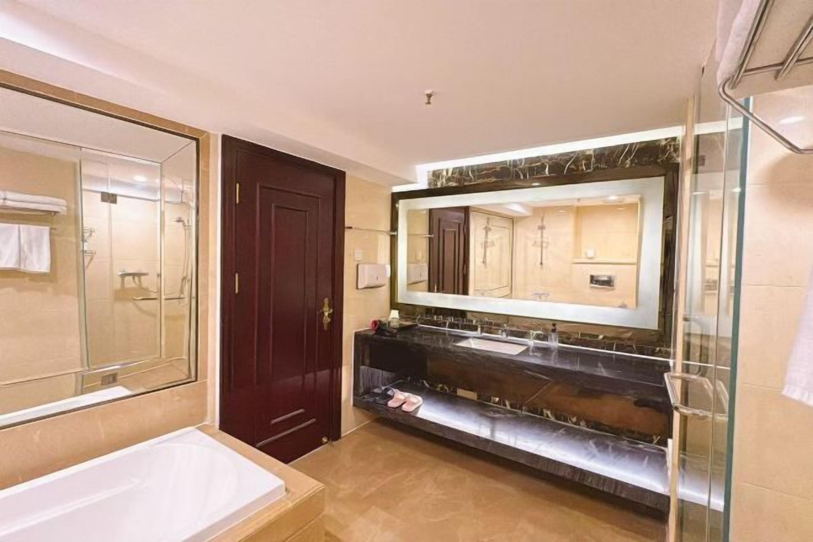 A bathroom with a large mirror, a bathtub, a vanity with a sink, and a shower area.