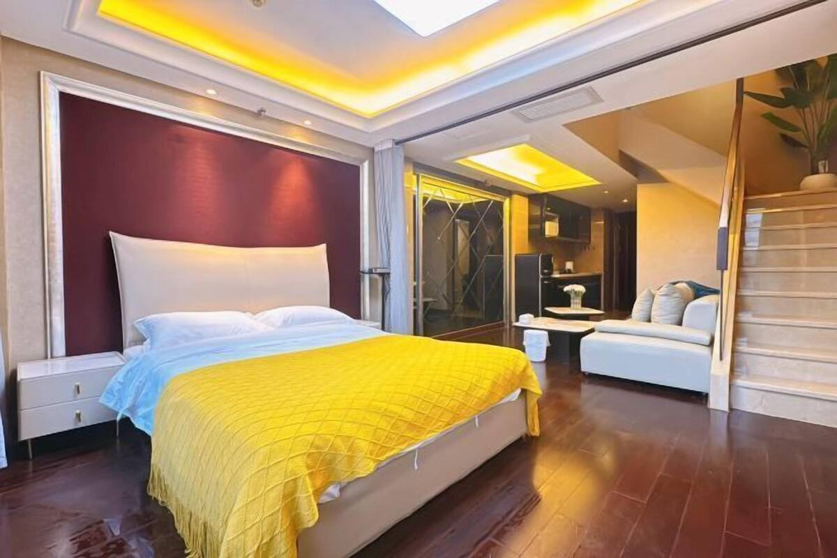 Una camera d'albergo moderna con un letto grande, un divano, un bagno con porta in vetro e una scala.