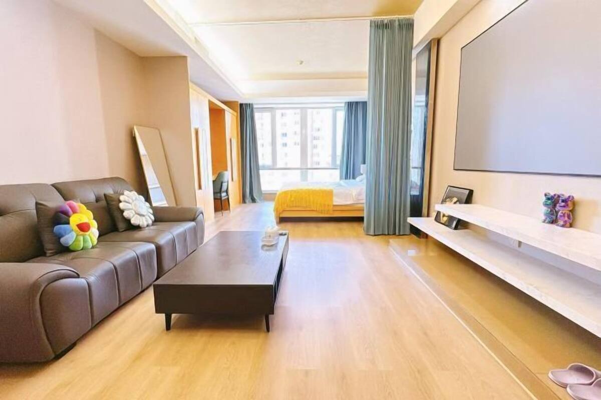 Una camera d'albergo moderna con divano, letto, tavolino, televisore e balcone vista edifici.