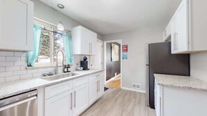 A modern kitchen with white cabinets, a stainless steel refrigerator, and a window with teal curtains. - Large Family Retreat in Quiet Denver Spot (Denver)