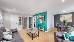 A modern living room with a teal accent wall, a dining area with a table and chairs, and a staircase leading to another level. - Large Family Retreat in Quiet Denver Spot (Denver)