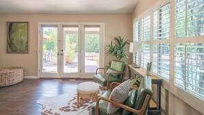 A spacious living area with a large sliding glass door leading to an outdoor patio, a green leather sofa, a round ottoman, and a wooden coffee table. - Scottsdale Treasure: Private Pool and Tranquil Yard Retreat! (Scottsdale)