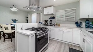 A modern kitchen with white cabinets, a built-in stove, and a dining area with a table and chairs. - Melrose Pet-Friendly 3BR. Feel like royalty (Vista)