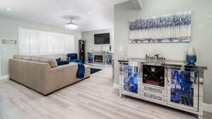 A modern living room with a beige sofa, a glass cabinet with blue decorative items, and a painting of trees on the wall. - Melrose Pet-Friendly 3BR. Feel like royalty (Vista)