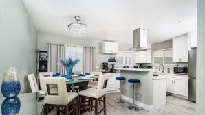 A modern kitchen with white cabinets, a stainless steel refrigerator, and a dining area with a glass table and chairs. - Melrose Pet-Friendly 3BR. Feel like royalty (Vista)