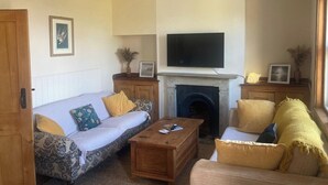 Ein Wohnzimmer mit einer Couch, Sesseln, einem Couchtisch, einem Kamin und einem Fernseher.
