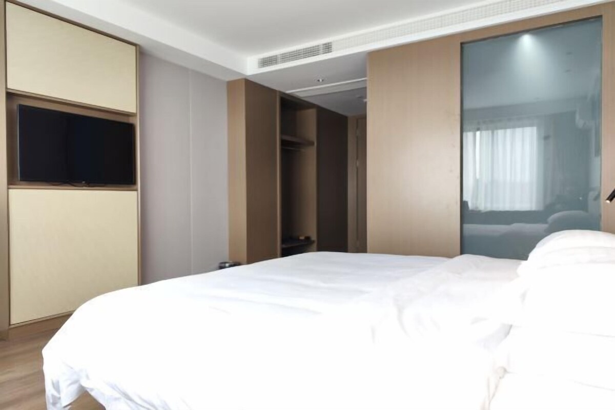 Una habitación de hotel con cama, televisión montada en la pared y armario corredero.