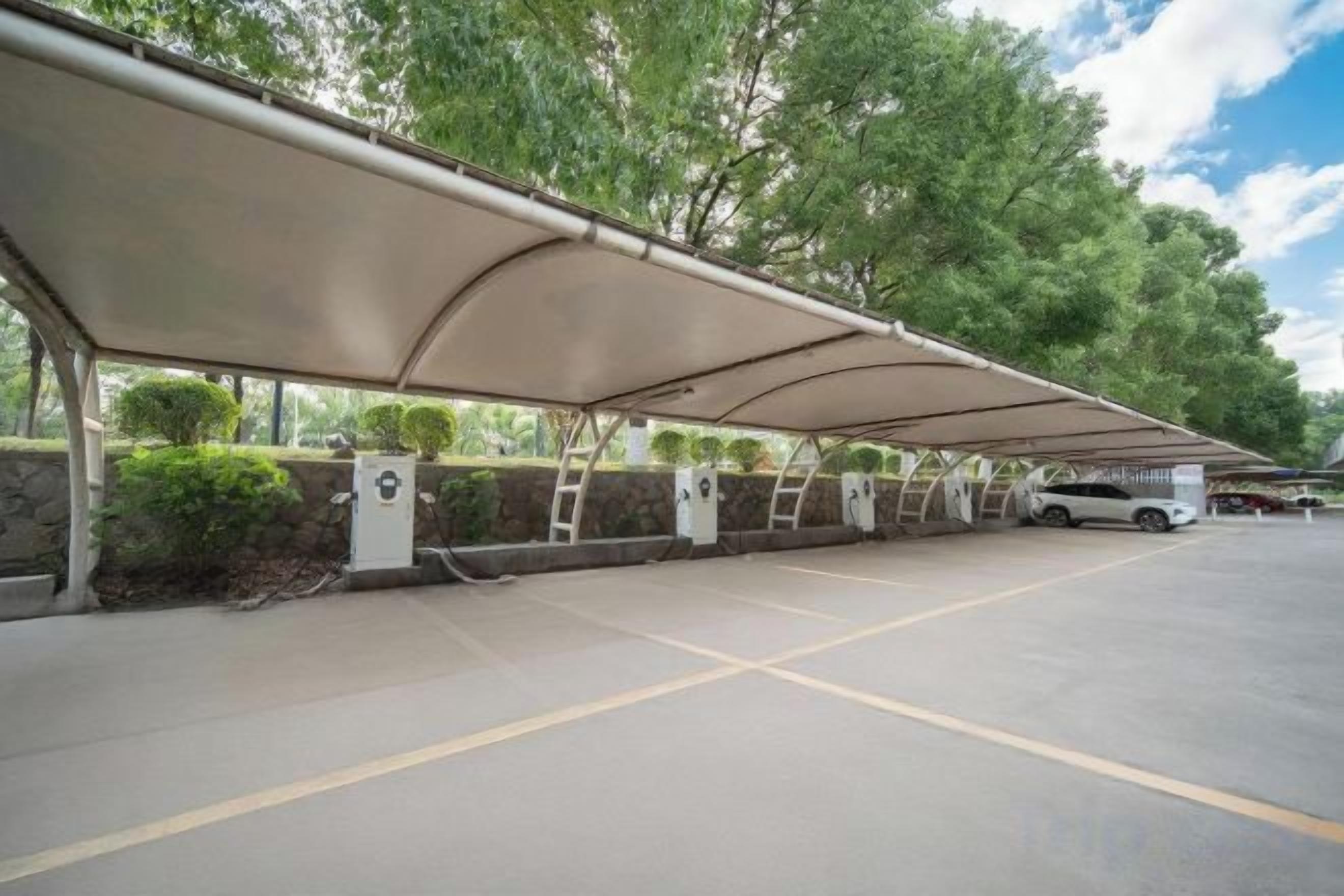 Un espace de stationnement doté de places de parking couvertes, d’un mur en pierre et d’arbres en arrière-plan.