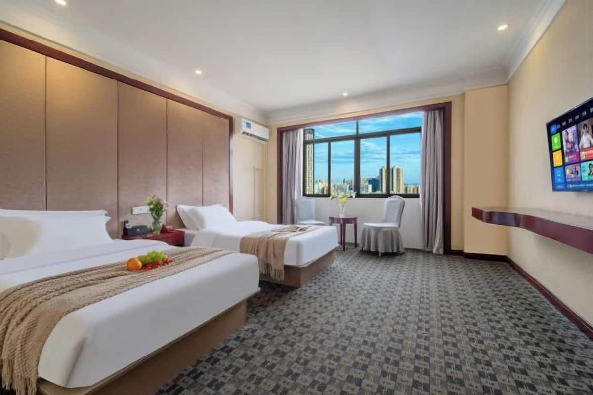 Una habitación de hotel con una cama grande, una cama más pequeña, un escritorio, una silla y un televisor en la pared.