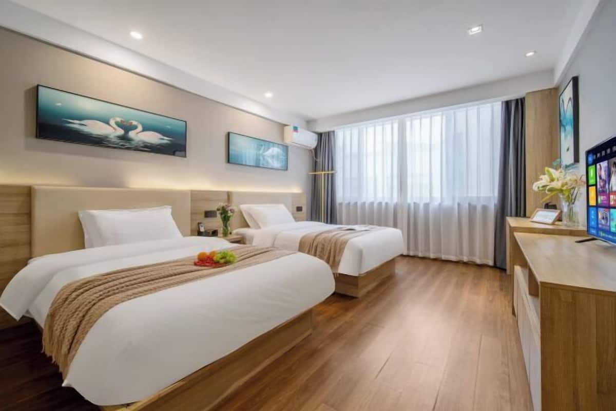 Habitación de hotel con dos camas, un escritorio, un televisor y obras de arte en las paredes.