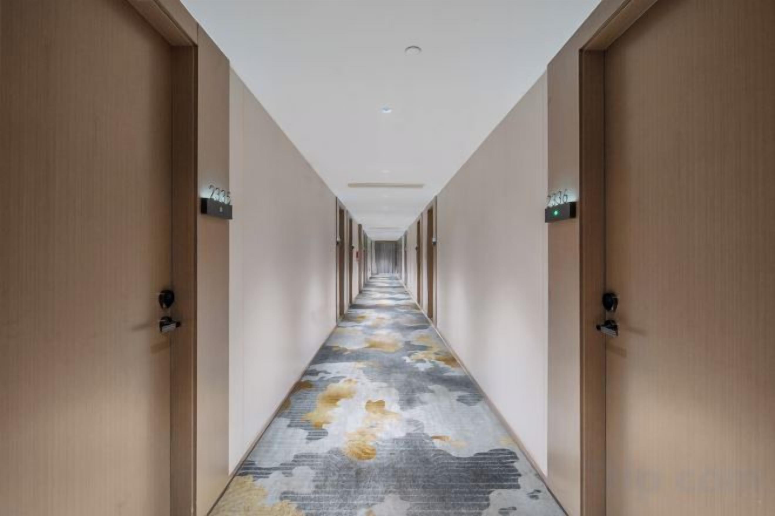 A hotel hallway with doors on both sides, a carpeted floor, and a ceiling light fixture.