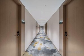 Corredor de hotel com portas em ambos os lados, piso coberto de carpete e luminária no teto.