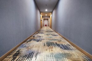 A hotel hallway with a patterned carpet, a red door at the end, and a light fixture on the ceiling. - Shaoxing Shangyu Baiyun Hotel (Shaoxing)