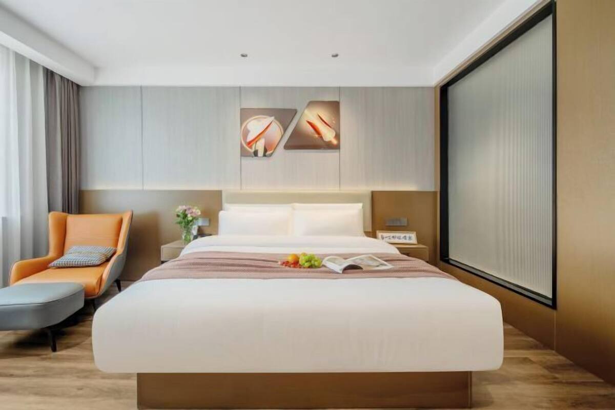 Una habitación de hotel moderna con una cama grande, una silla, una mesita de noche y un ventanal amplio.