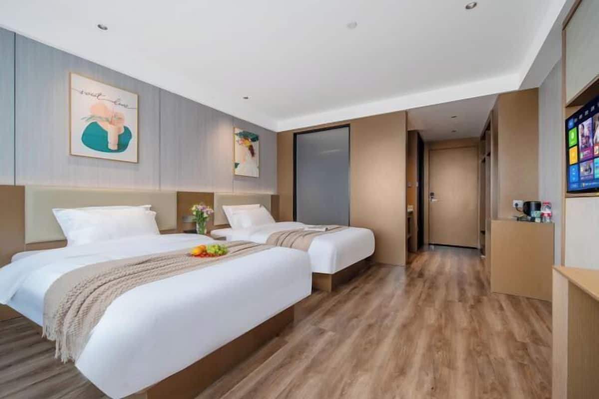 Habitación de hotel moderna con dos camas, piso de madera, un ventanal grande y un televisor en la pared.