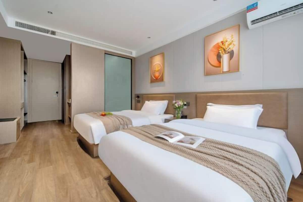 Habitación de hotel con dos camas, piso de madera, un ventanal grande y un cuadro en la pared.