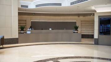 A modern hotel lobby with a curved reception desk, potted plants, and a digital directory display.