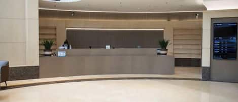 Un moderno vestíbulo de hotel con un mostrador de recepción curvo, plantas en macetas y una pantalla digital de directorio.
