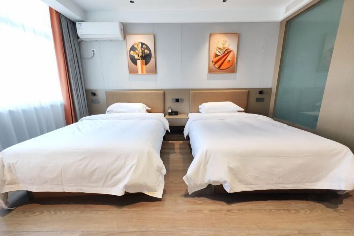Habitación de hotel con dos camas individuales, un ventanal con cortinas y dos cuadros colgados en la pared.