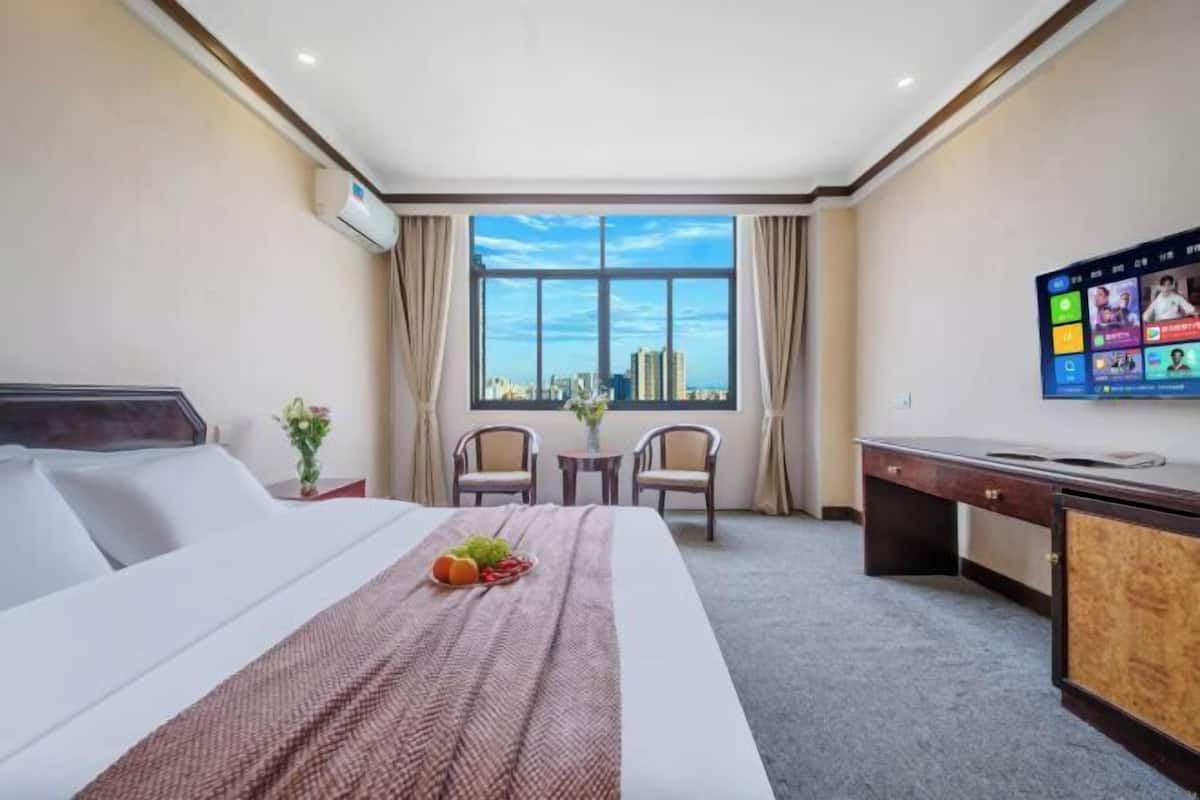 Habitación de hotel con cama, escritorio, televisor, ventana con vistas a la ciudad y una pequeña mesa con sillas.
