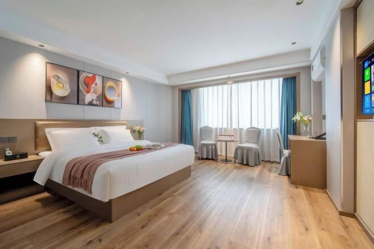 Habitación de hotel moderna con una cama grande, un escritorio, una silla, una mesita y un ventanal con cortinas.
