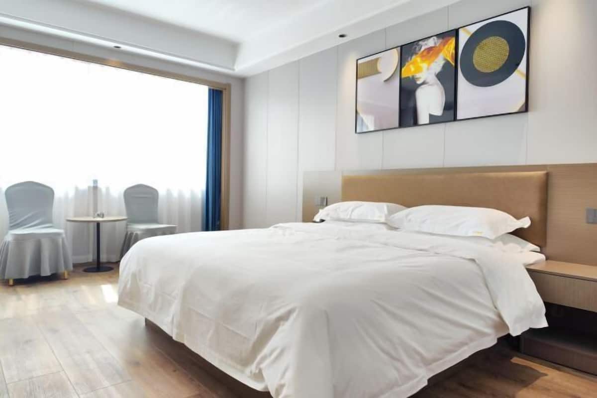 Habitación de hotel moderna con una cama grande, una mesita de noche, una silla y vistas a la ciudad.