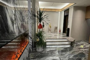 A modern lobby with a marble floor, a bench, and potted plants.