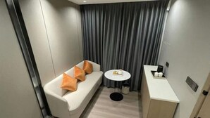 A modern hotel room with a white sofa, a small round table, and a minibar.