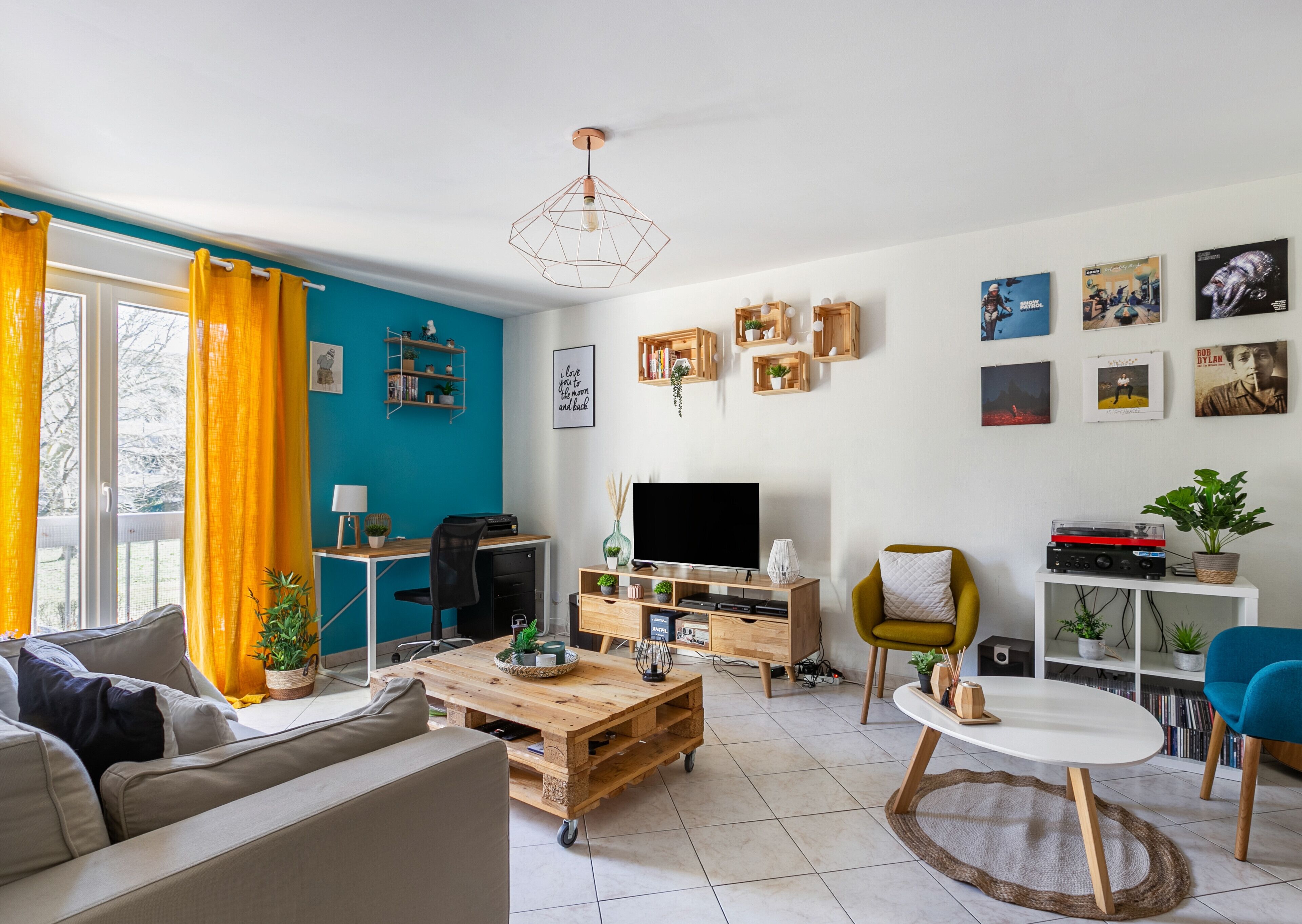 A modern living room with a blue accent wall, a wooden coffee table, a sofa, a TV, and a bookshelf.