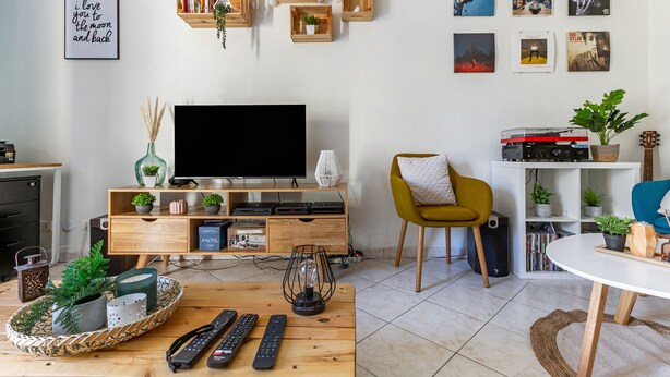 Un saló modern amb televisió de pantalla plana, prestatges de fusta amb objectes decoratius, un butac armchair groc i una zona de menjador amb taula rodona.