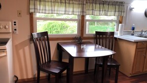 A kitchen with a dining table, two chairs, a window with a view of greenery, a white countertop, a sink, and a stove. - The Meadow Cabin at Horn Cabins in Manns Choice PA (Manns Choice)
