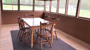 A covered dining area with a wooden table and chairs, large windows, and a ceiling fan. - The Meadow Cabin at Horn Cabins in Manns Choice PA (Manns Choice)