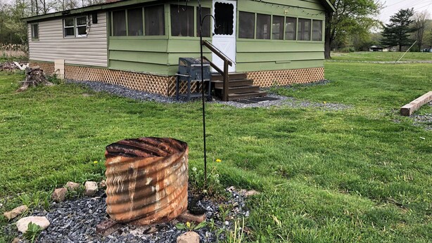 A small, single-story house with a green exterior and a red roof, surrounded by a grassy yard and trees. - The Meadow Cabin at Horn Cabins in Manns Choice PA (Manns Choice)