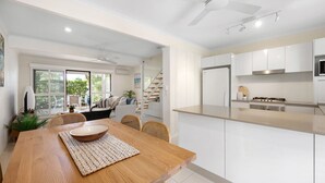 Une cuisine moderne avec des meubles blancs, un îlot central et un coin repas comprenant une table et des chaises en bois.