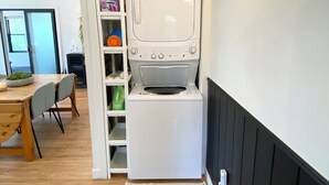 Een wasserij met een witte wasmachine en droger, een gestreept tapijt en een plank met wasmiddelen.