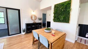Een eetgedeelte met een houten tafel, stoelen, een spiegel en een groene wanddecoratie.