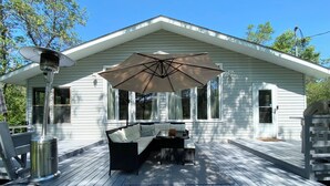 Een overdekt terras buiten met een bank en tafel, een terrasverwarmer en een grote parasol.