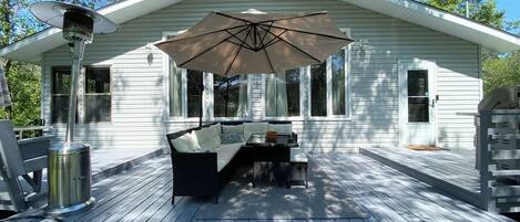 A covered outdoor deck with a sofa and table, a patio heater, and a large umbrella.