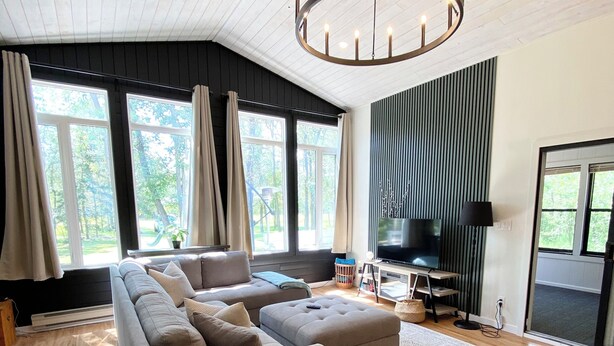 Een moderne woonkamer met een hoekbank, een rond hockertje en een groot raam met gordijnen.