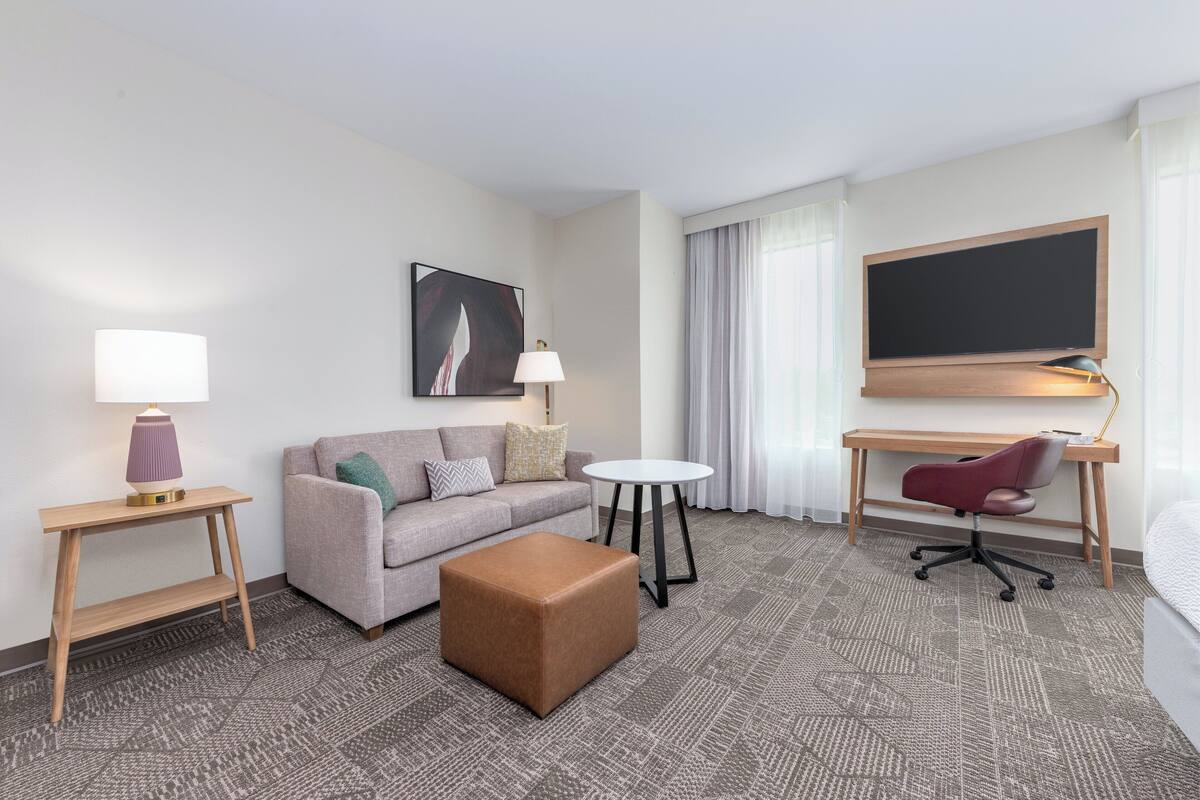 A hotel room with a sofa, a small table, a desk with a chair, a large bed, and a TV.