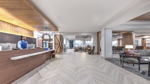 A modern hotel lobby with a wooden reception desk, a herringbone-patterned floor, and a seating area with sofas and a coffee table. - Staybridge Suites Port Arthur by IHG (Port Arthur)