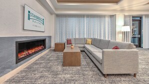 A modern hotel room with a fireplace, a grey sofa, a coffee table, and a sign indicating Staybridge suites at An IHG hotel. - Staybridge Suites Port Arthur by IHG (Port Arthur)