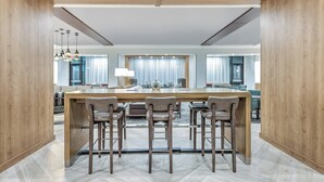 A spacious dining area with a large wooden table and four bar stools. The room features a modern design with wooden walls and a herringbone floor pattern. - Staybridge Suites Port Arthur by IHG (Port Arthur)